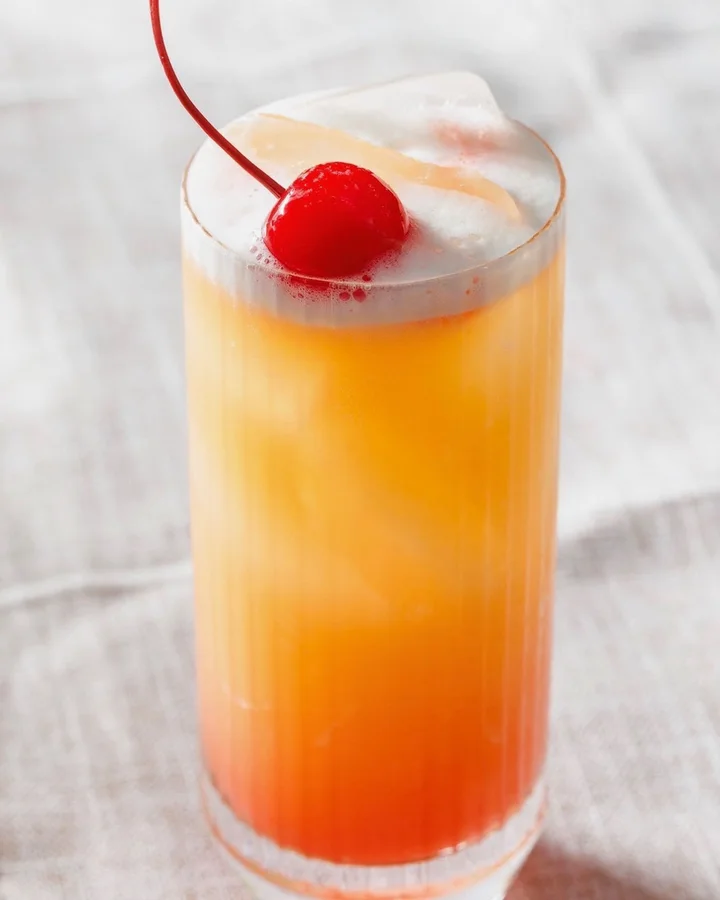 Tequila Sunrise in a tall glass with a maraschino cherry