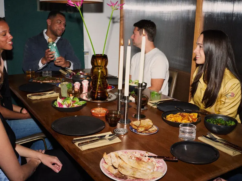 Friends around the dinner table, one holding up a bottle of De Nada Blanco