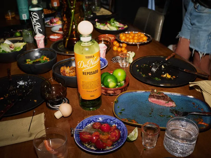 A bottle of De Nada Reposado on the dinner table with tajín grapefruit and a jalapeño margarita