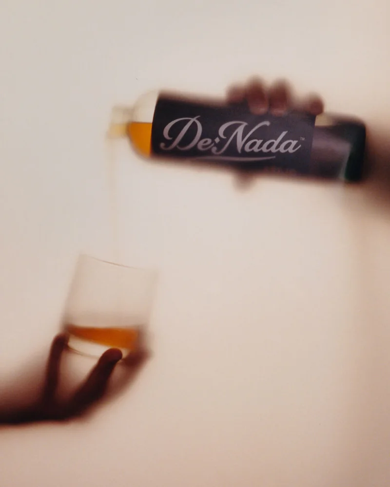 A hand pouring De Nada Añejo into a rocks glass, soft focus on film